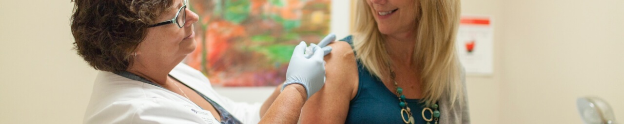 A nurse administers a flu shot in a female patient's upper arm.